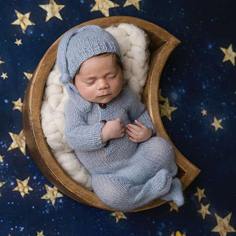 Newborn baby boy wearing light blue photographed in a wood moon-shaped bowl against a starry night background in Connecticut.