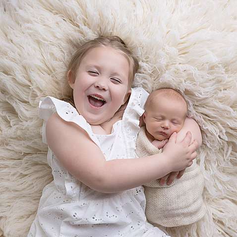 Studio baby photo with a baby boy and sibling laying on a white flokati rug in Connecticut.
